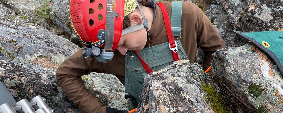 A person wearing a climbing helmet and headlamp secures a safety rope.